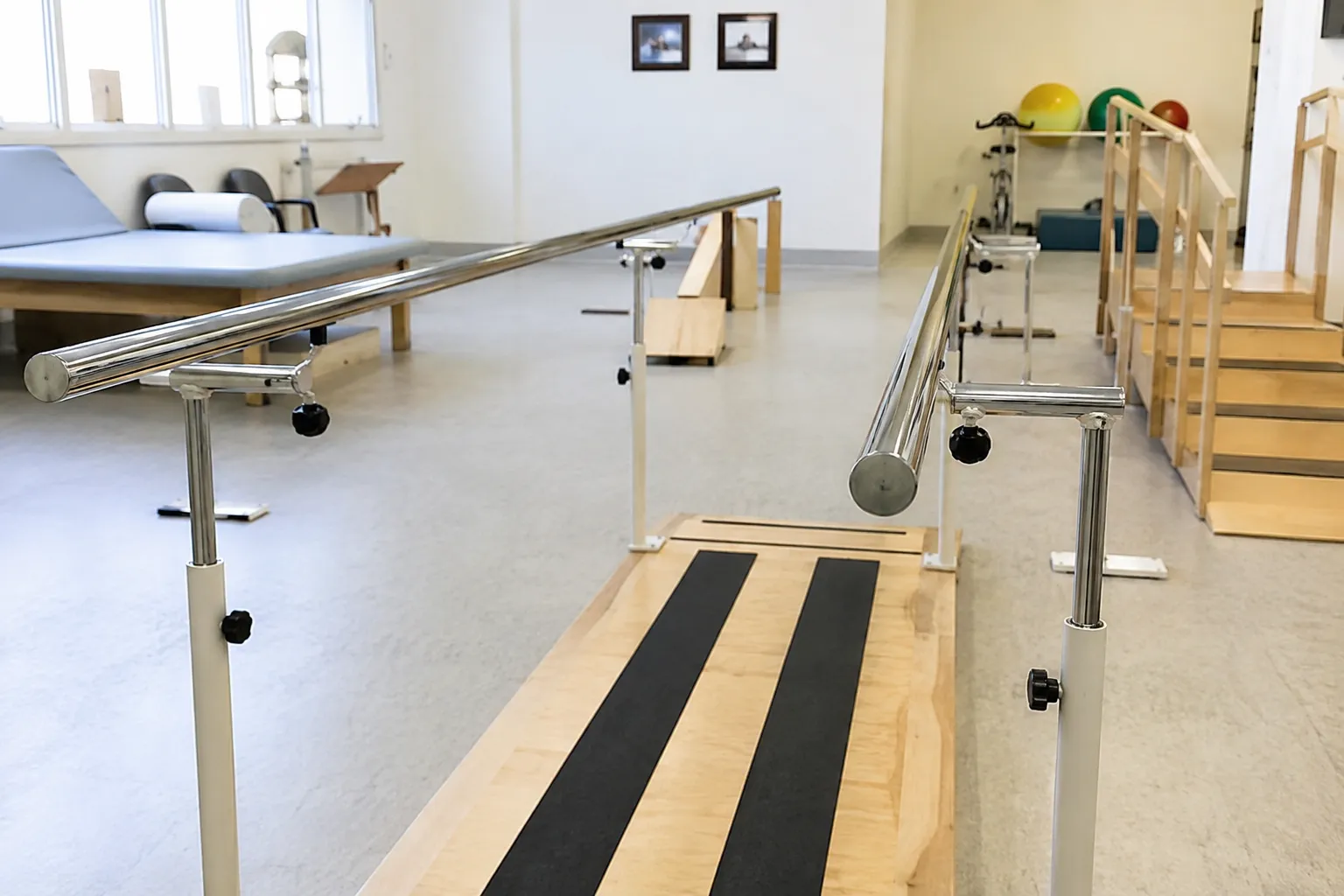 Patient walking between height-adjustable parallel bars while a physiotherapist supervises gait
